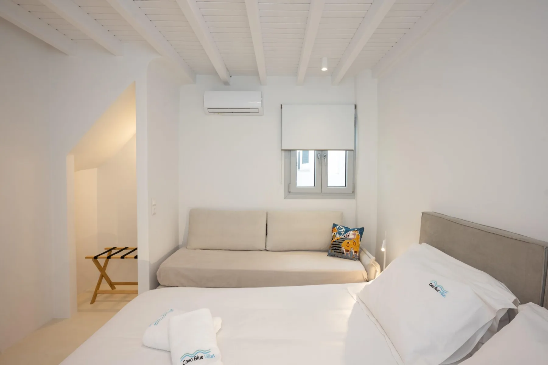Un dormitorio con una cama grande y otra más pequeña bajo una ventana.