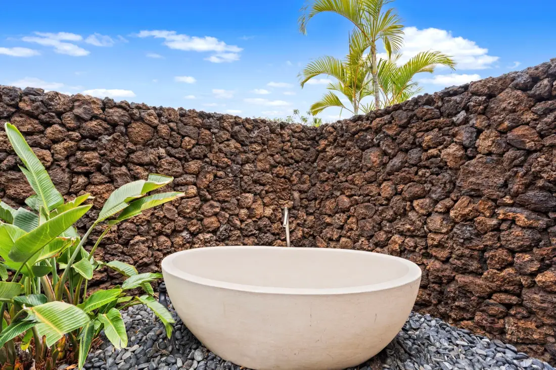 Una bañera exterior está entre plantas tropicales junto a un muro de piedra.