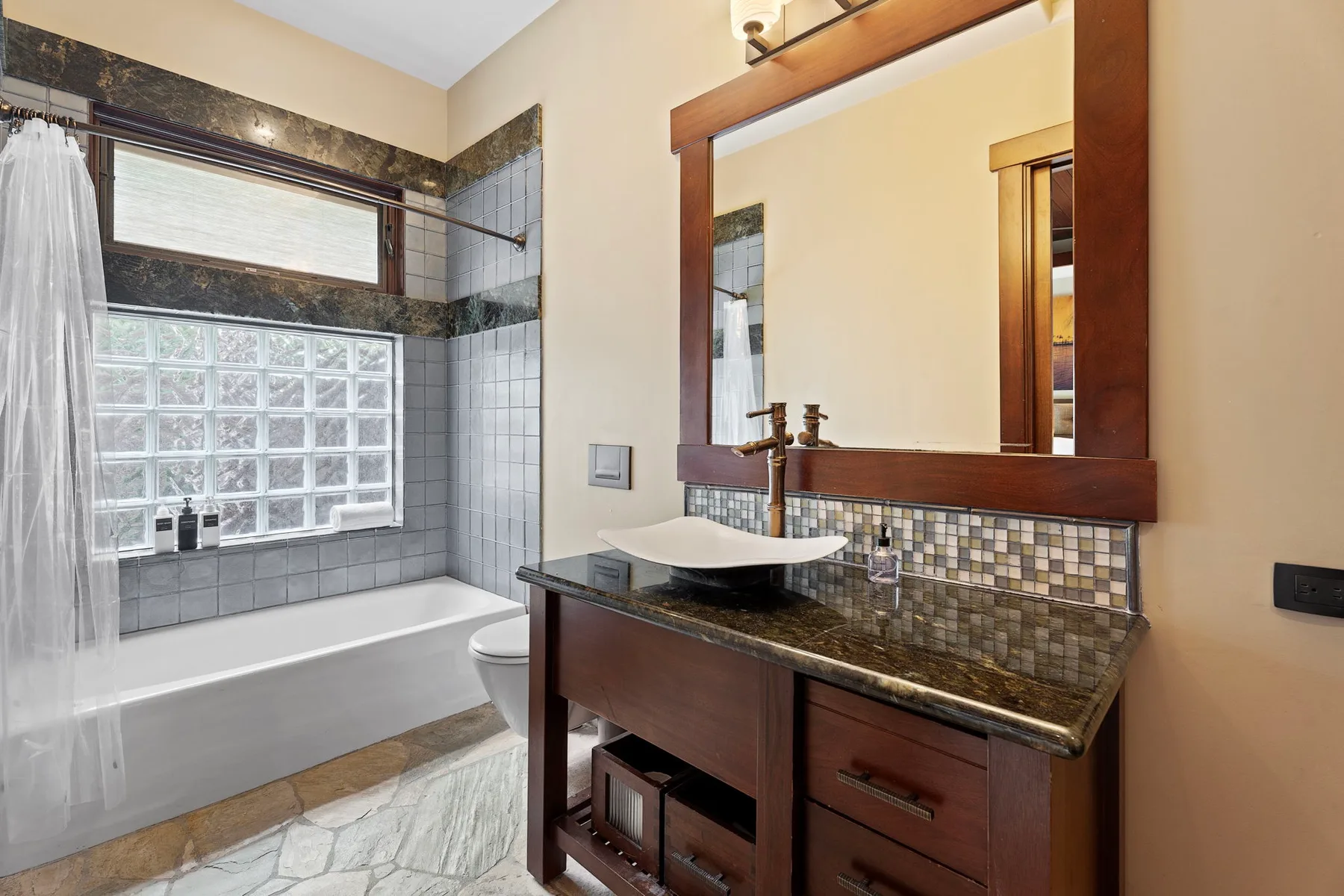 Un baño con bañera y un mueble oscuro con lavabo sobre encimera.