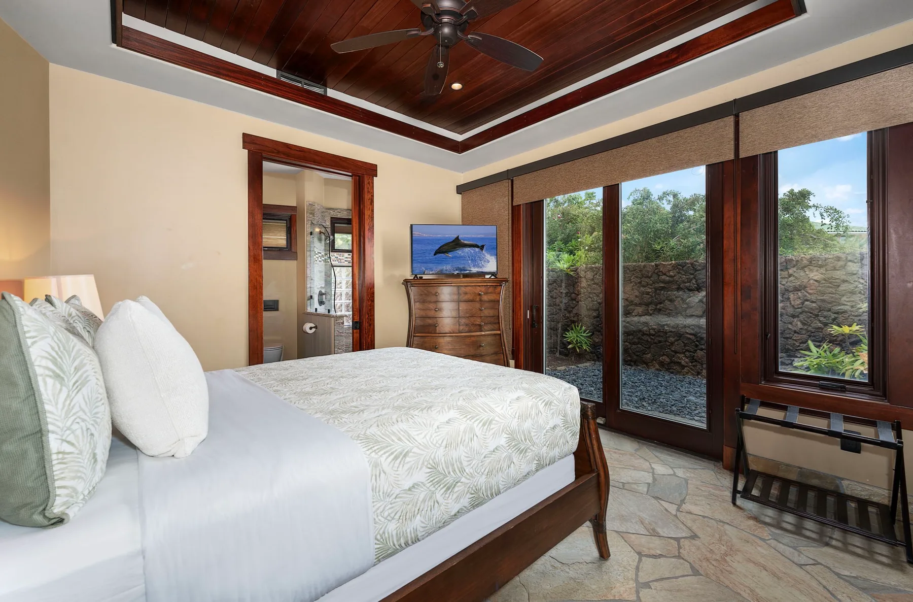 Un dormitorio con cama, techo de madera y grandes ventanas con vistas a la vegetación.