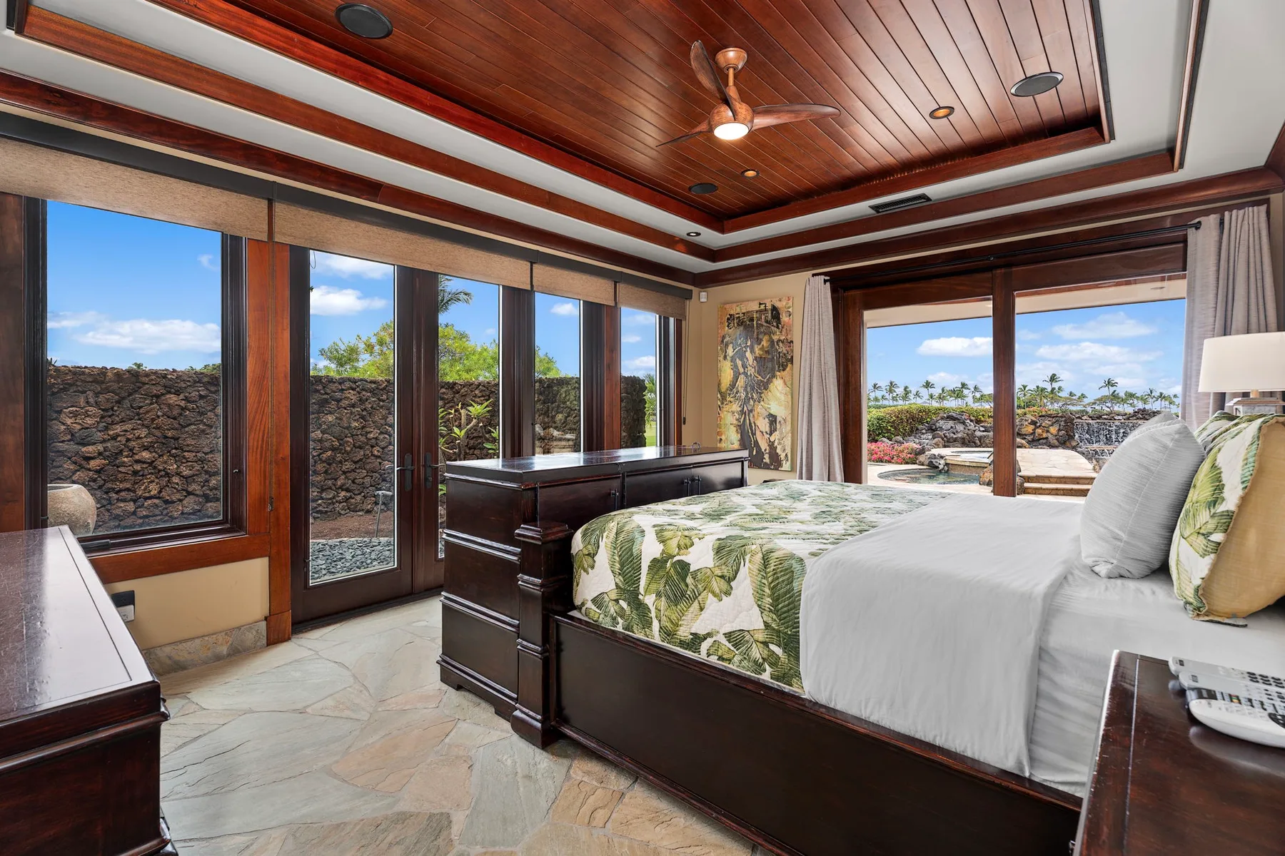 Un dormitorio con una cama grande, muebles de madera oscura y amplias ventanas que dan a un patio.