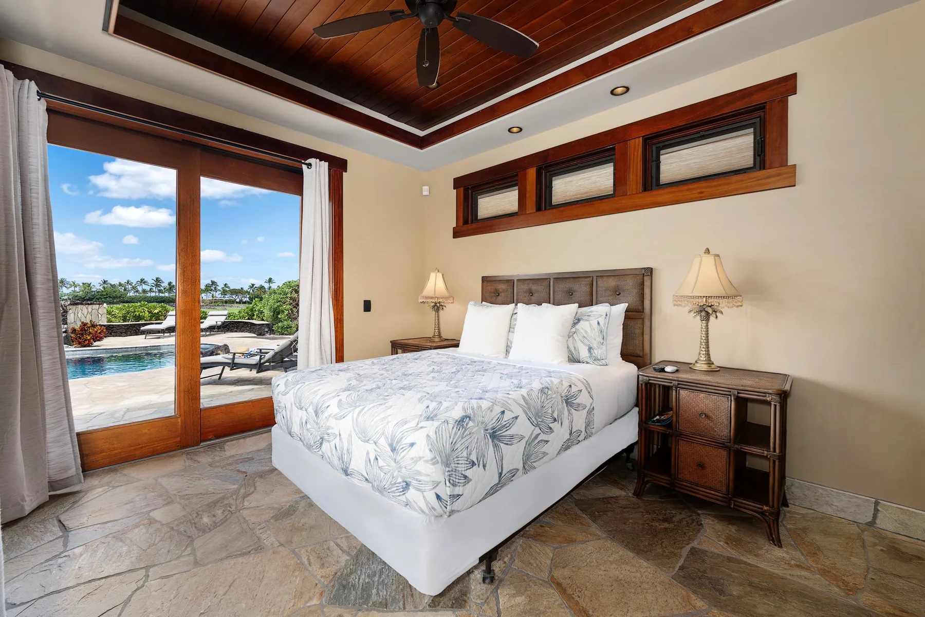 Un dormitorio con una cama, mesas de noche y puertas de vidrio con vista a la piscina.
