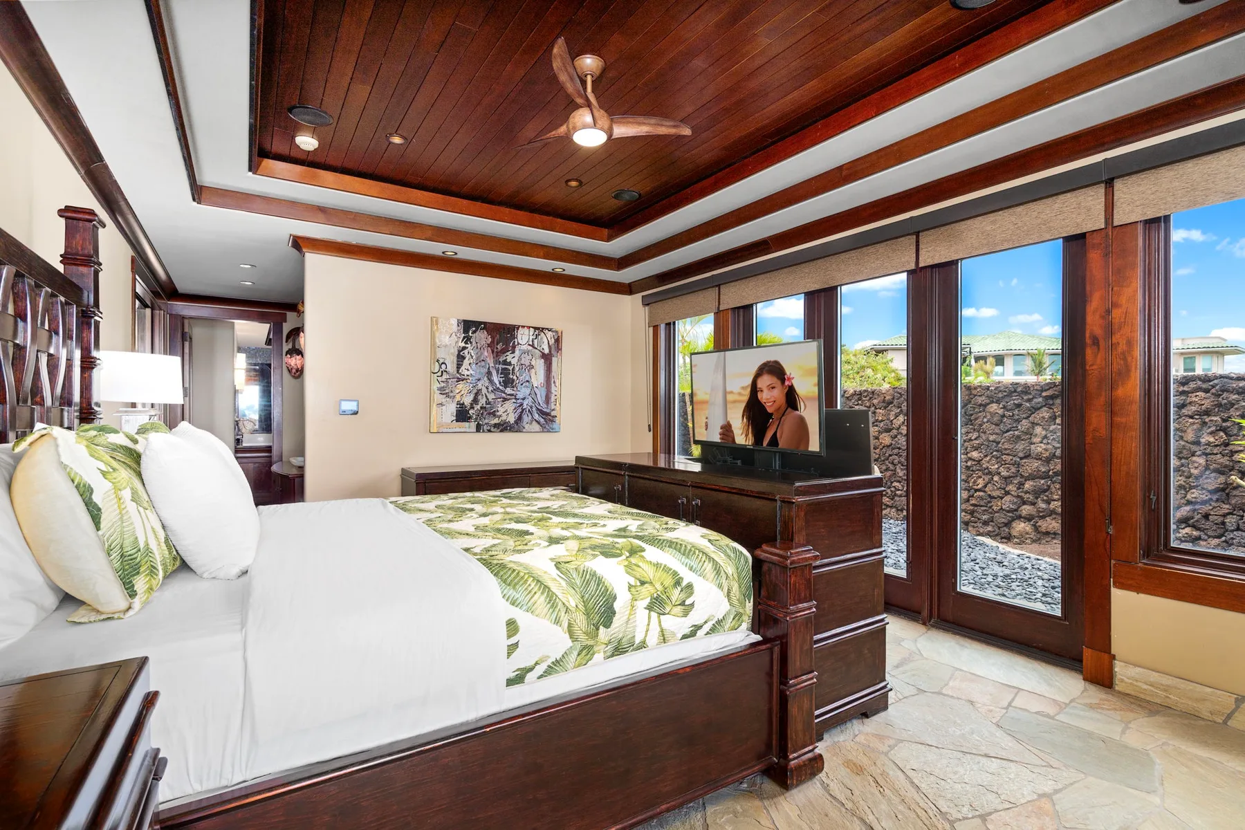 Un dormitorio con una cama grande, ropa de cama estampada y ventanas con vista a un muro de piedra exterior.