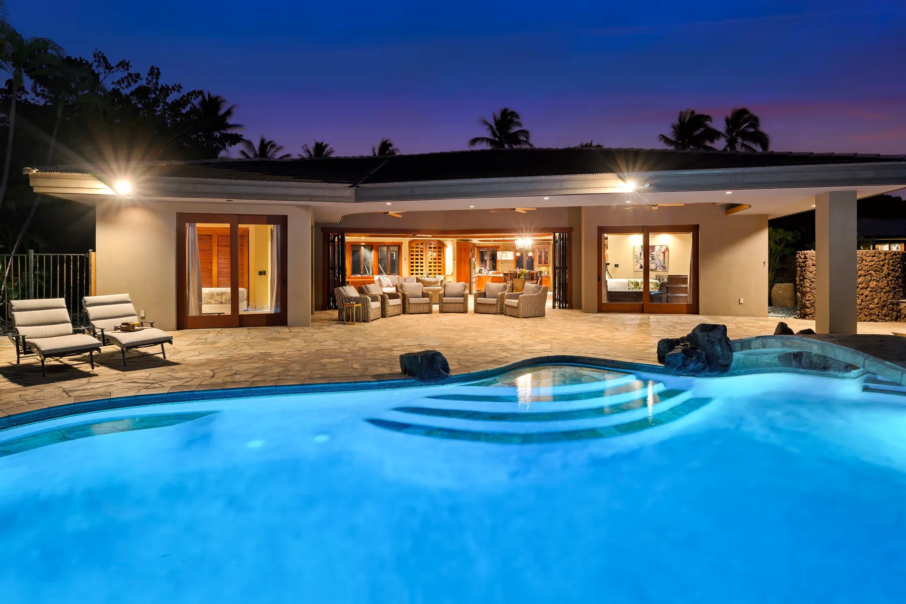 Un patio iluminado con una zona de estar da a una piscina al anochecer.