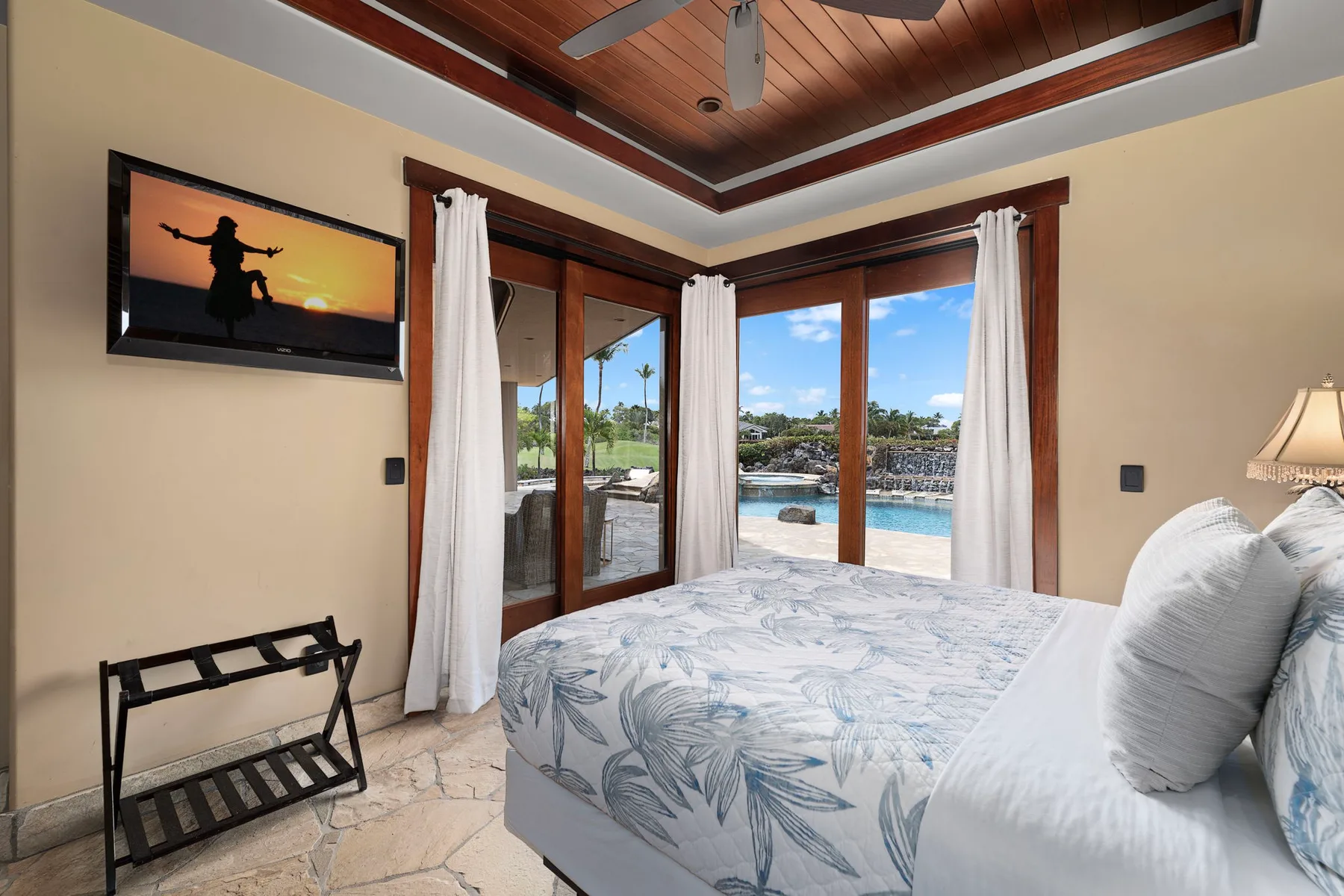 Un dormitorio con una cama junto a puertas de vidrio con vistas a una piscina y un jardín.