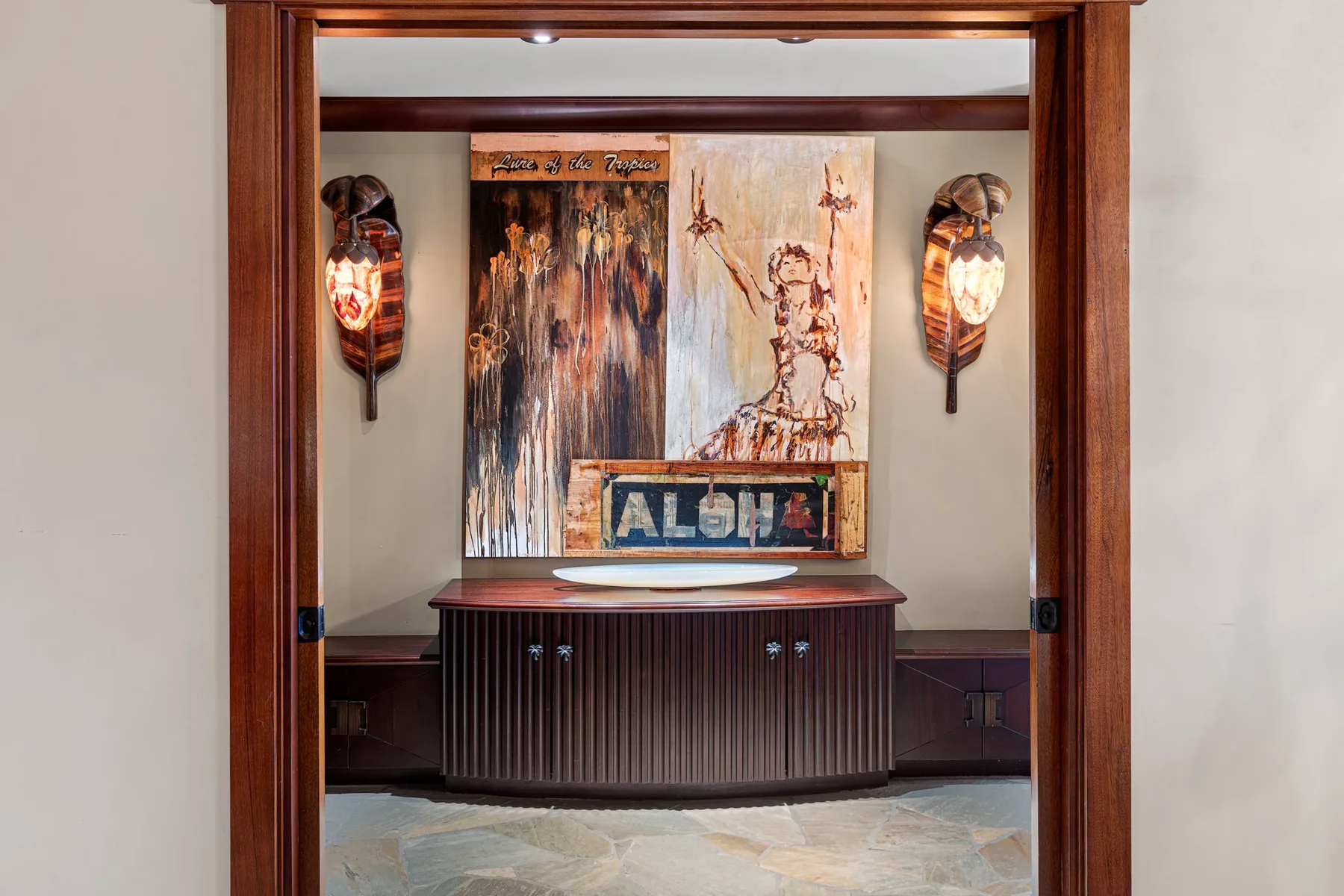Un tocador de madera oscura está bajo arte decorativo, enmarcado por una puerta de madera.