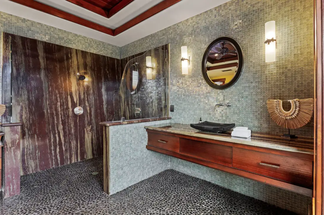 Un baño con un largo tocador de madera, un espejo redondo y una ducha.