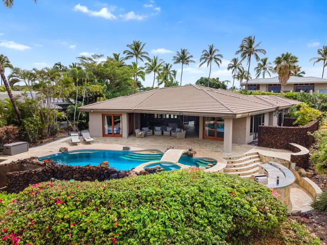 Una casa de poca altura da a una piscina curva entre jardines tropicales.