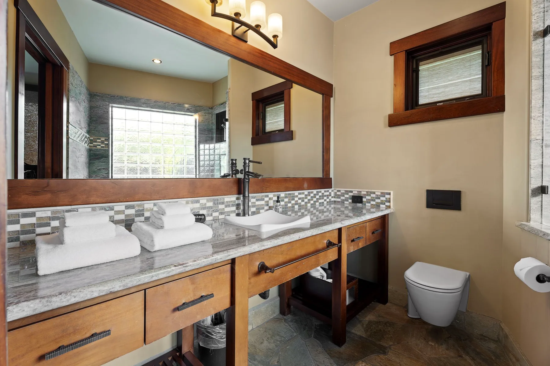 Un tocador de baño con un espejo amplio, dos lavabos y un inodoro.