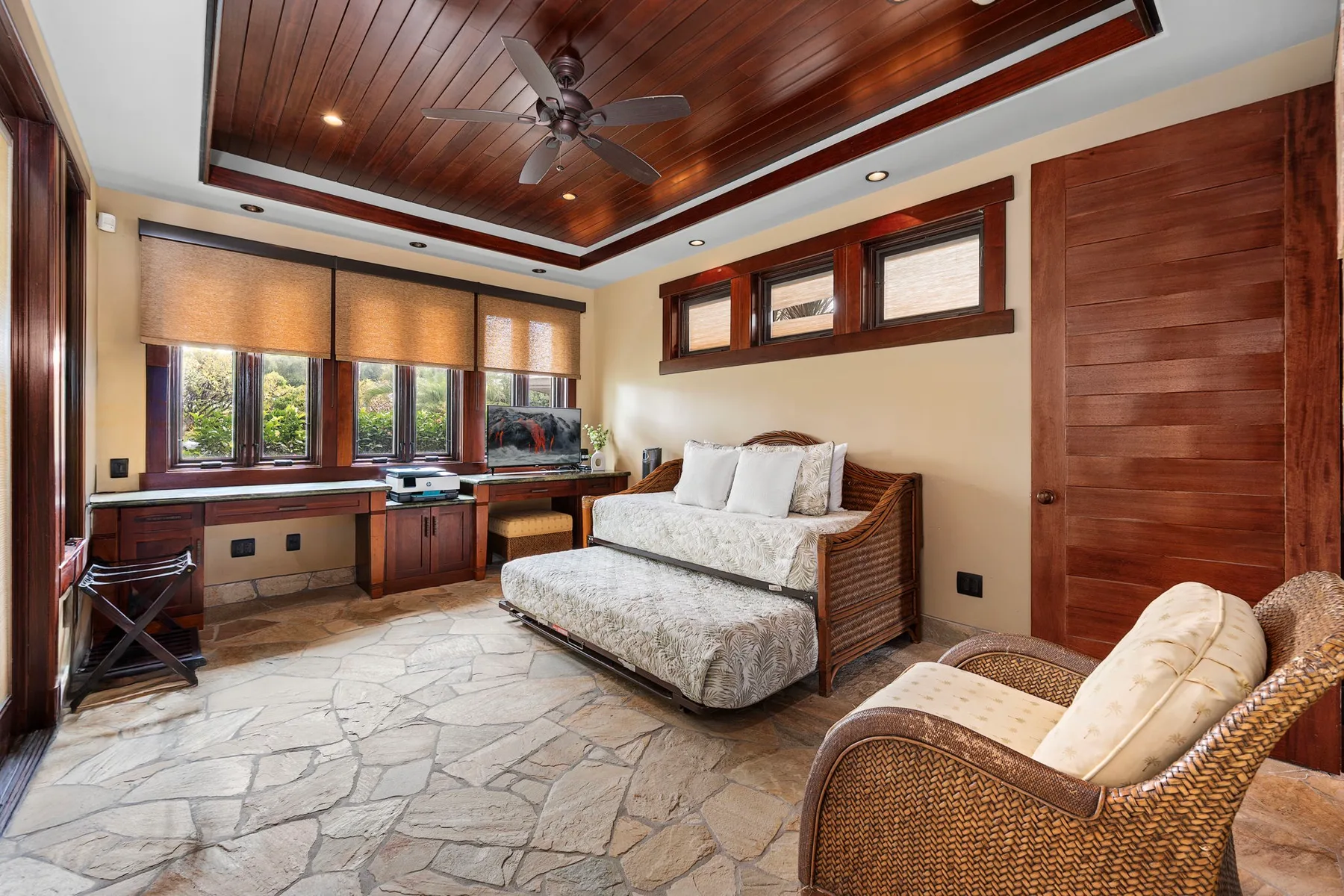 Un dormitorio con cama, escritorio y asientos tejidos bajo un techo revestido de madera.