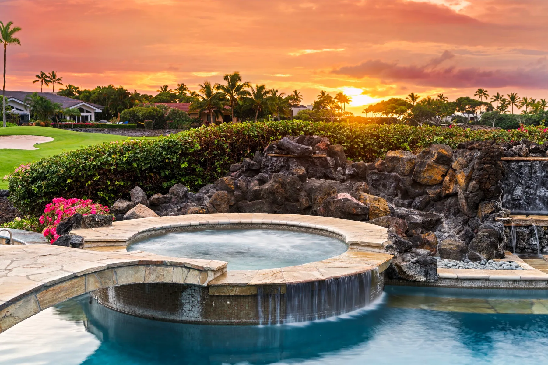 Una piscina al aire libre y un spa circular están junto a un jardín rocoso al atardecer.