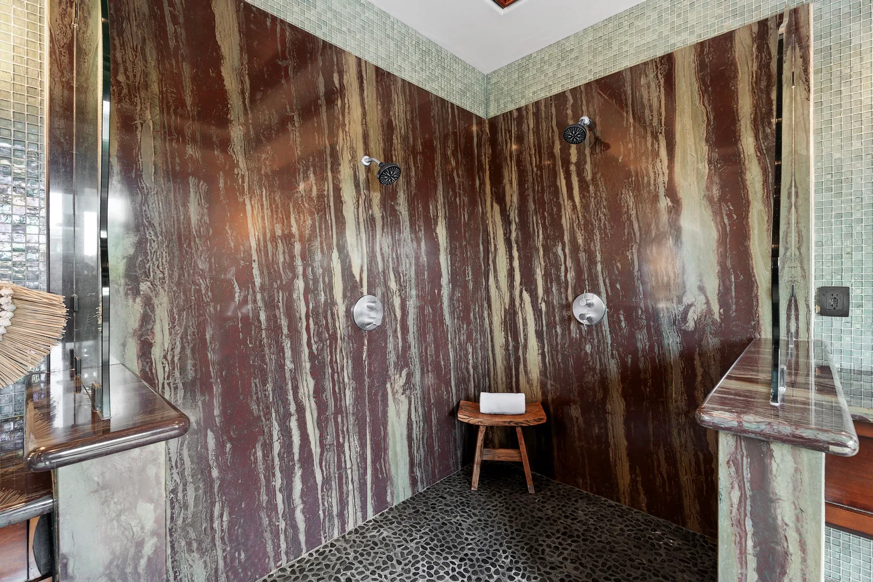 Zona de ducha con paredes oscuras estampadas y un pequeño taburete de madera.