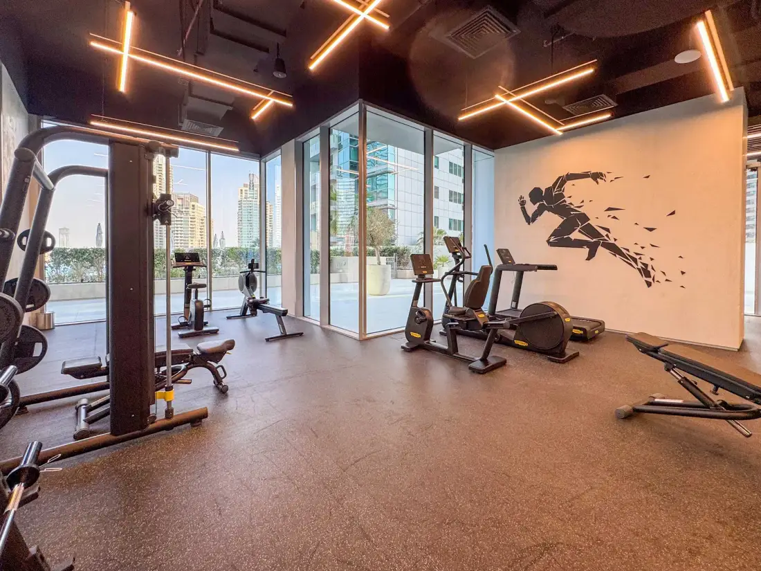 Un gimnasio con máquinas de ejercicio junto a ventanales.