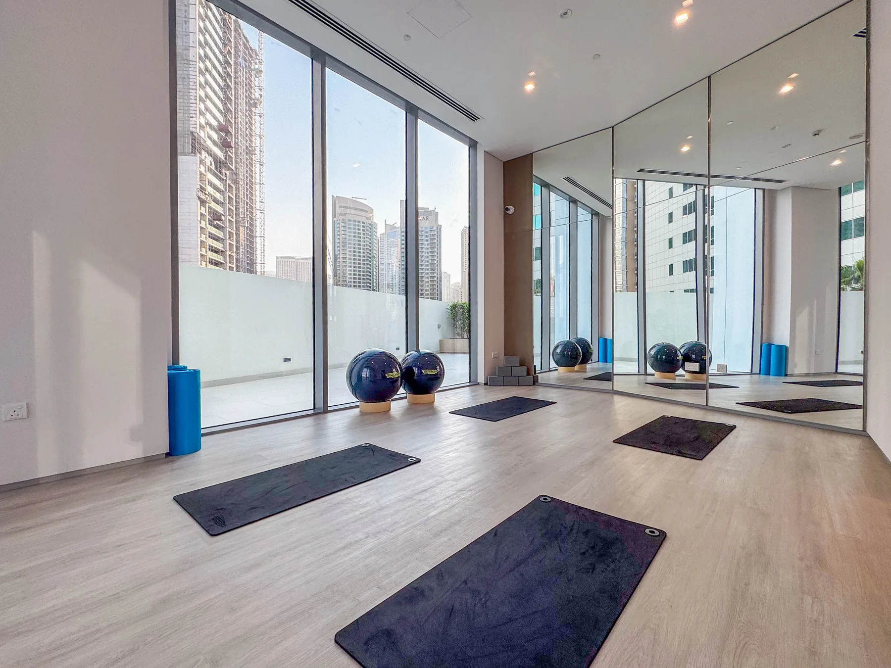 Una sala de ejercicio luminosa con colchonetas y grandes ventanas con vistas a edificios cercanos.