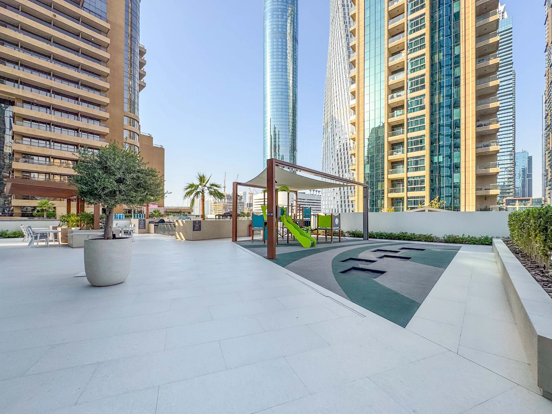 Un área de juegos al aire libre con un tobogán verde está entre edificios residenciales altos.