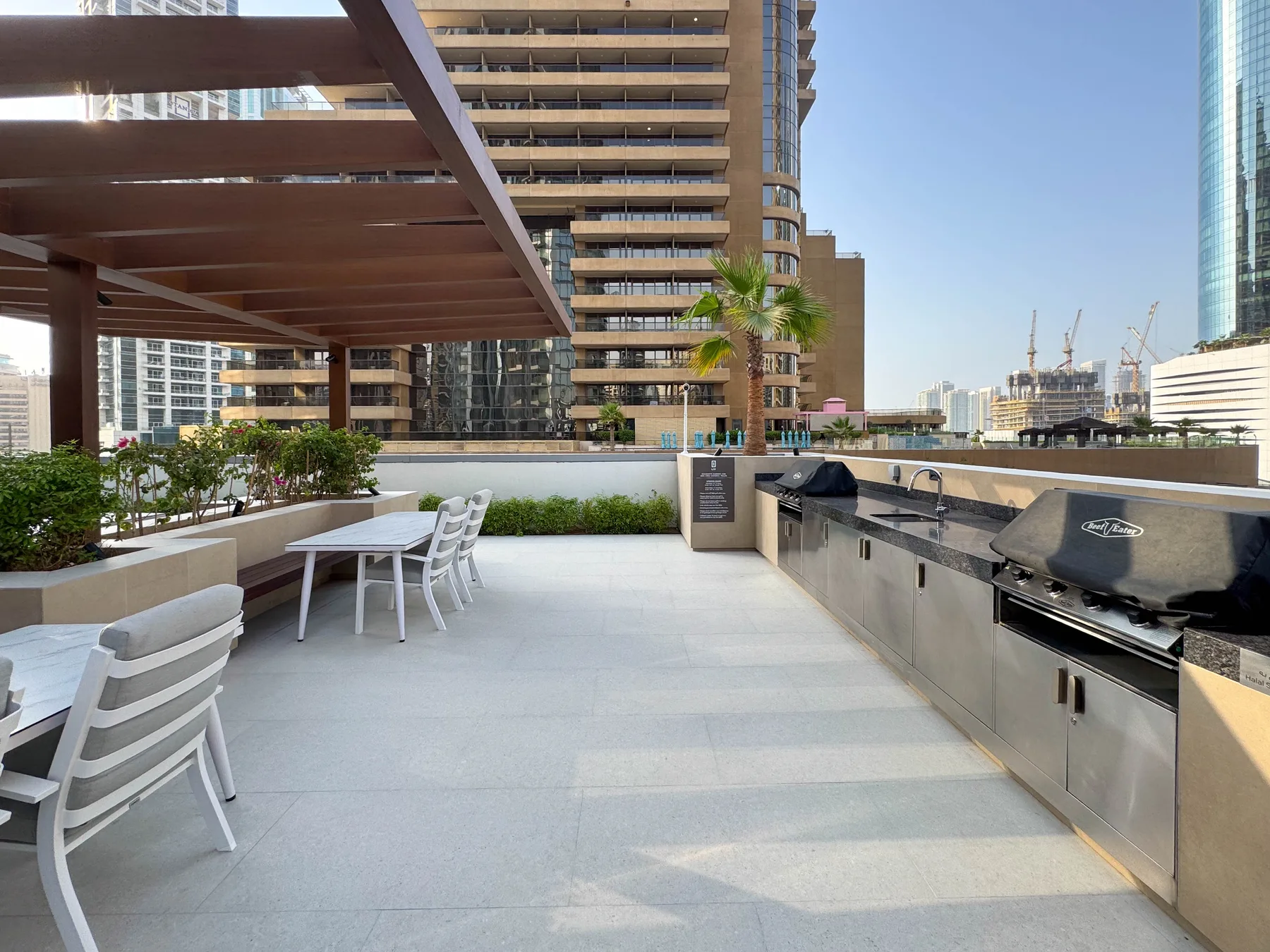 Una terraza exterior con una encimera larga, parrillas y asientos bajo una pérgola.