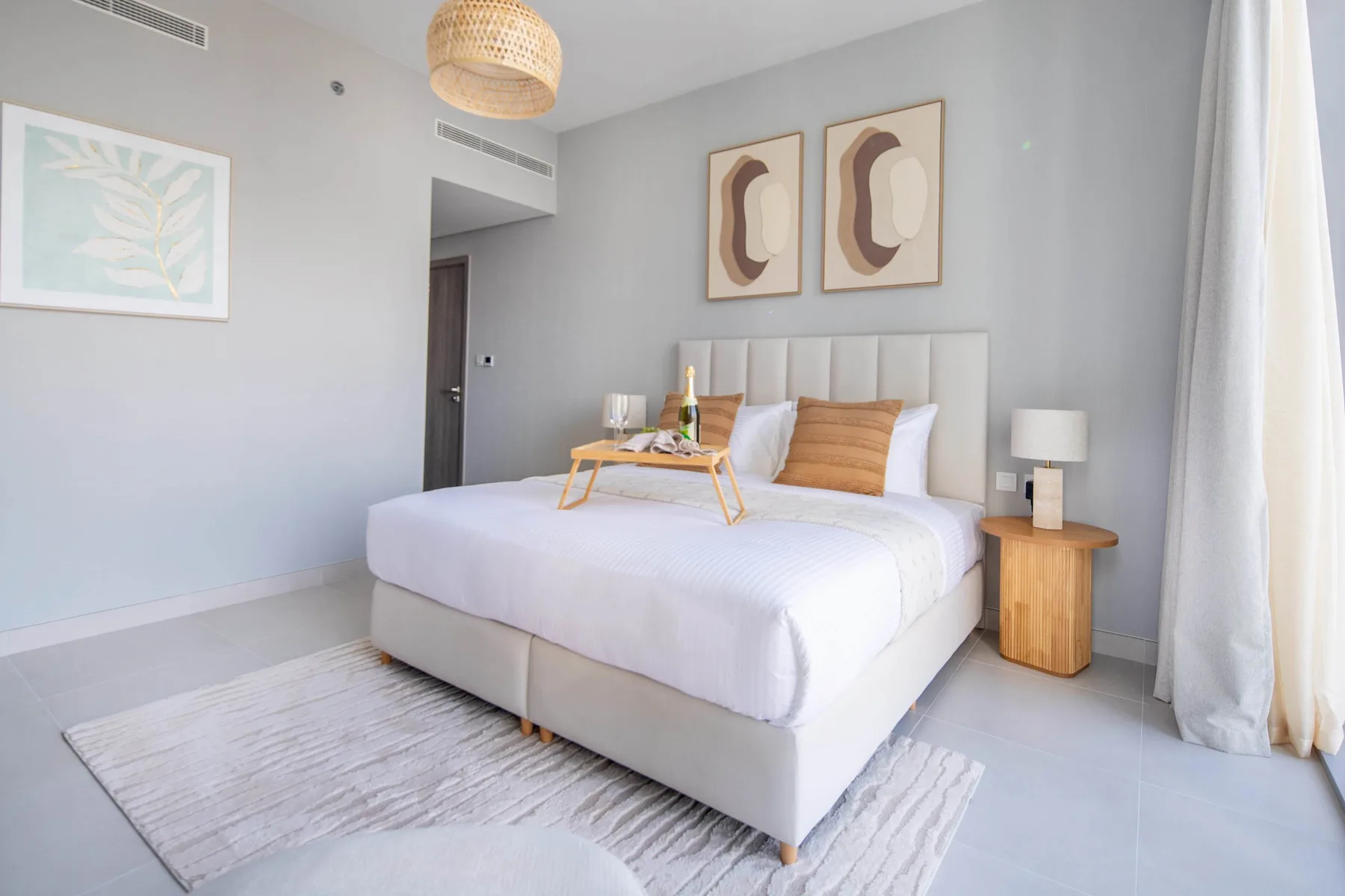 Un dormitorio luminoso con una cama tendida, mesitas de noche y cuadros enmarcados.
