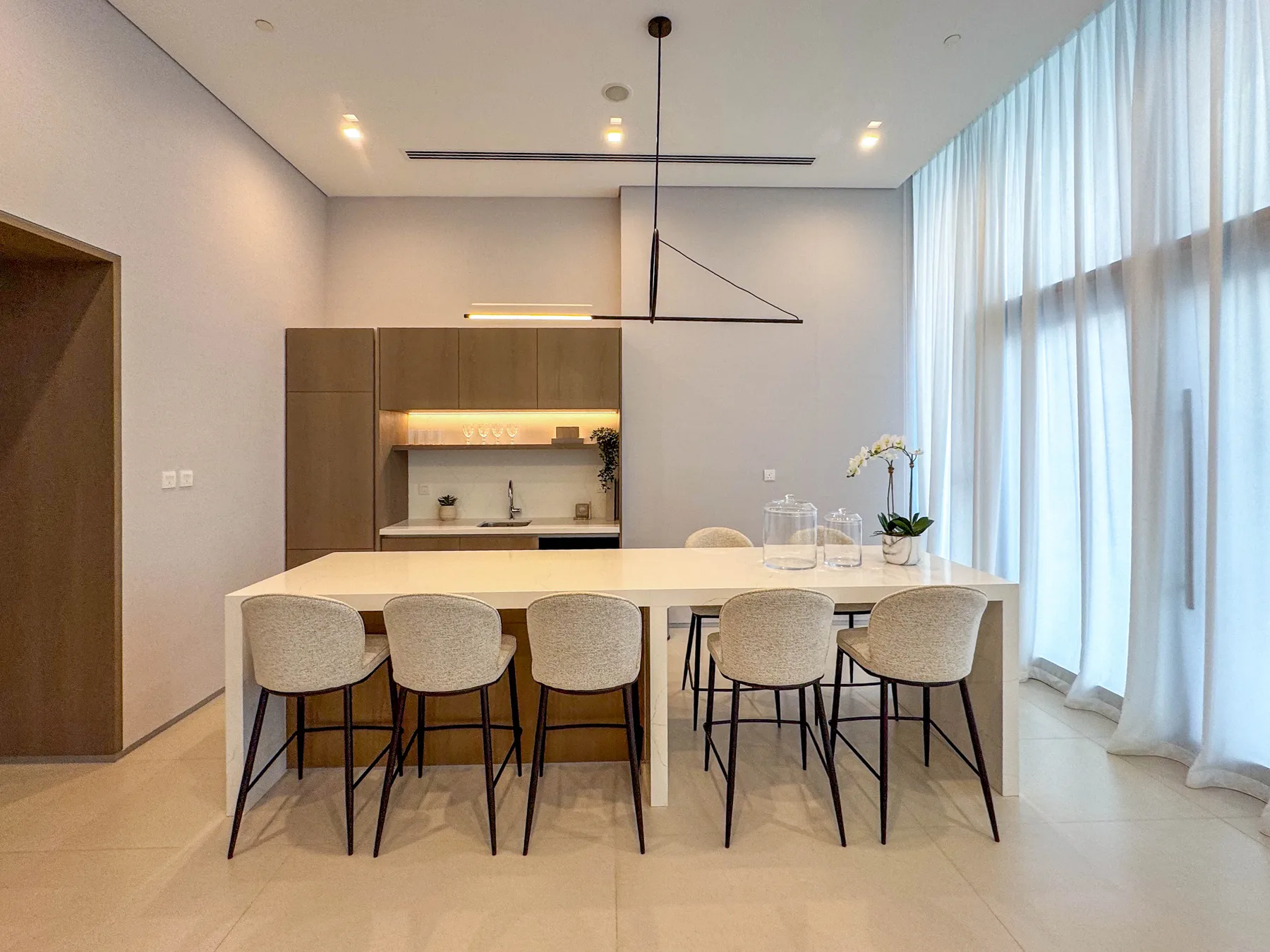 Un comedor luminoso con una mesa larga, varias sillas y cortinas de piso a techo.