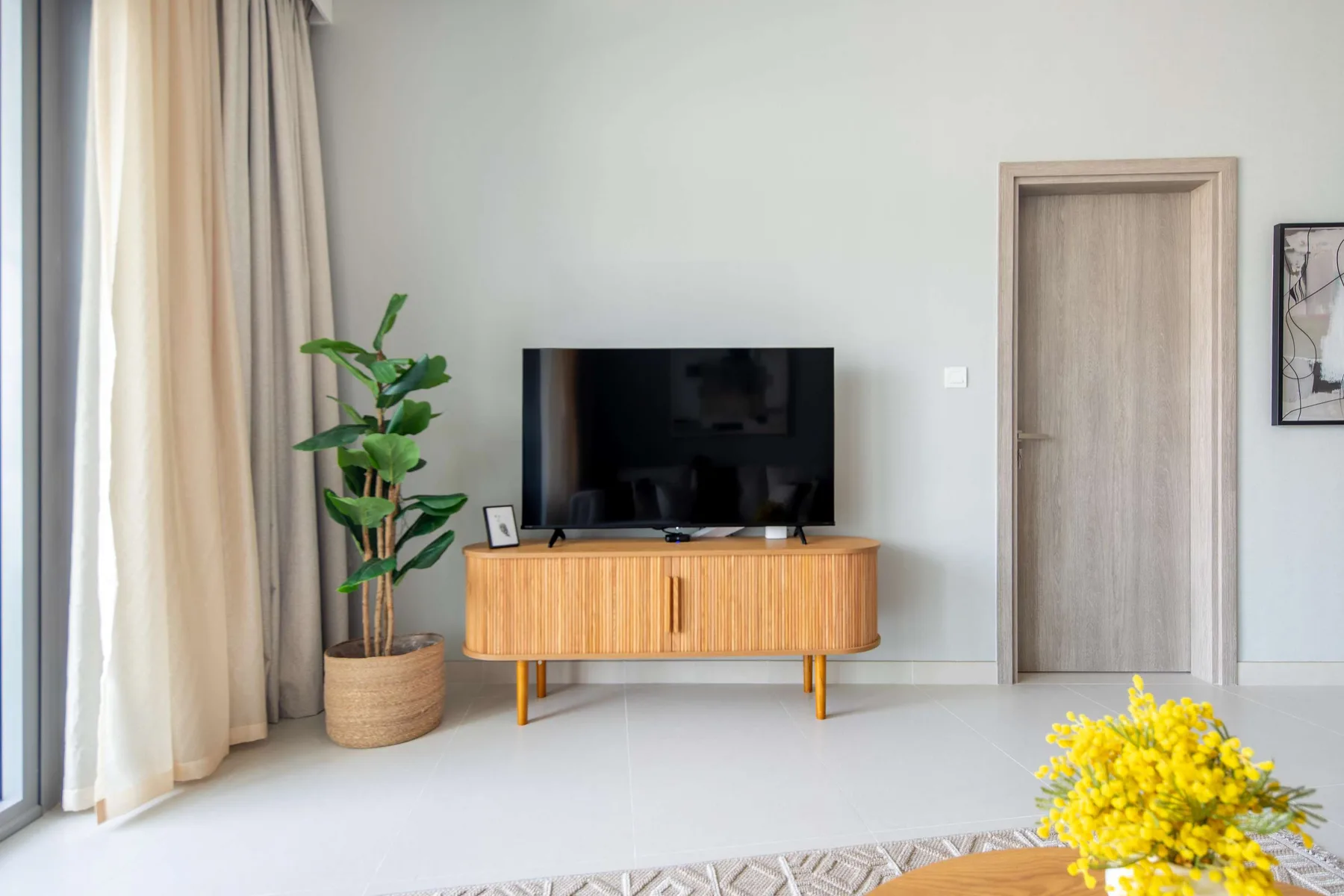 Una sala luminosa con un televisor sobre una consola de madera y una planta en maceta.