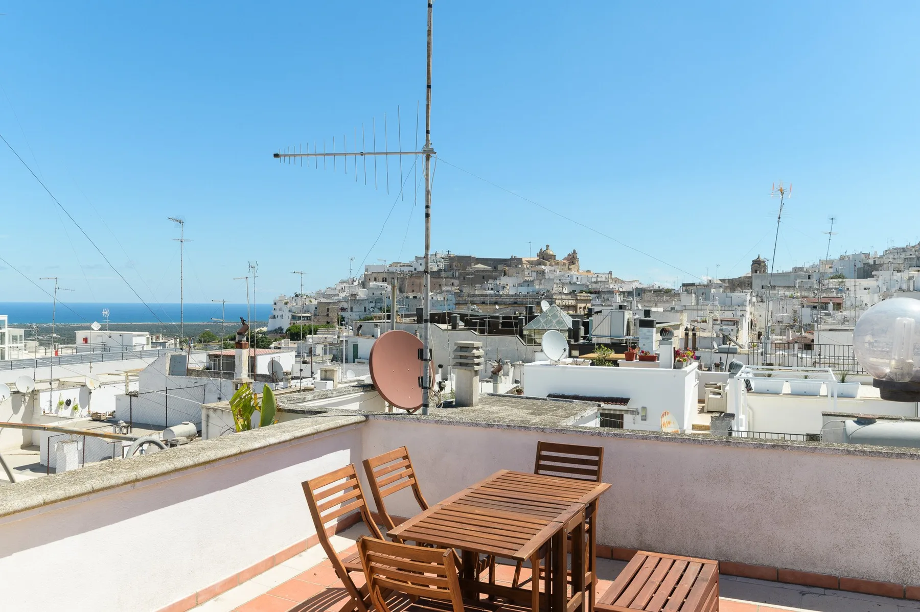 A rooftop terrace with wooden seating overlooks a coastal town and the sea.
