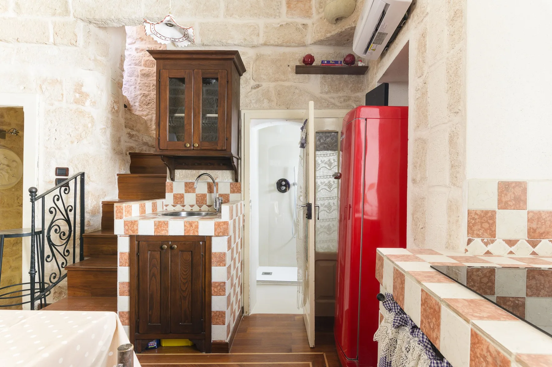 Una zona de cocina con azulejos, armarios de madera, un fregadero y un refrigerador rojo.