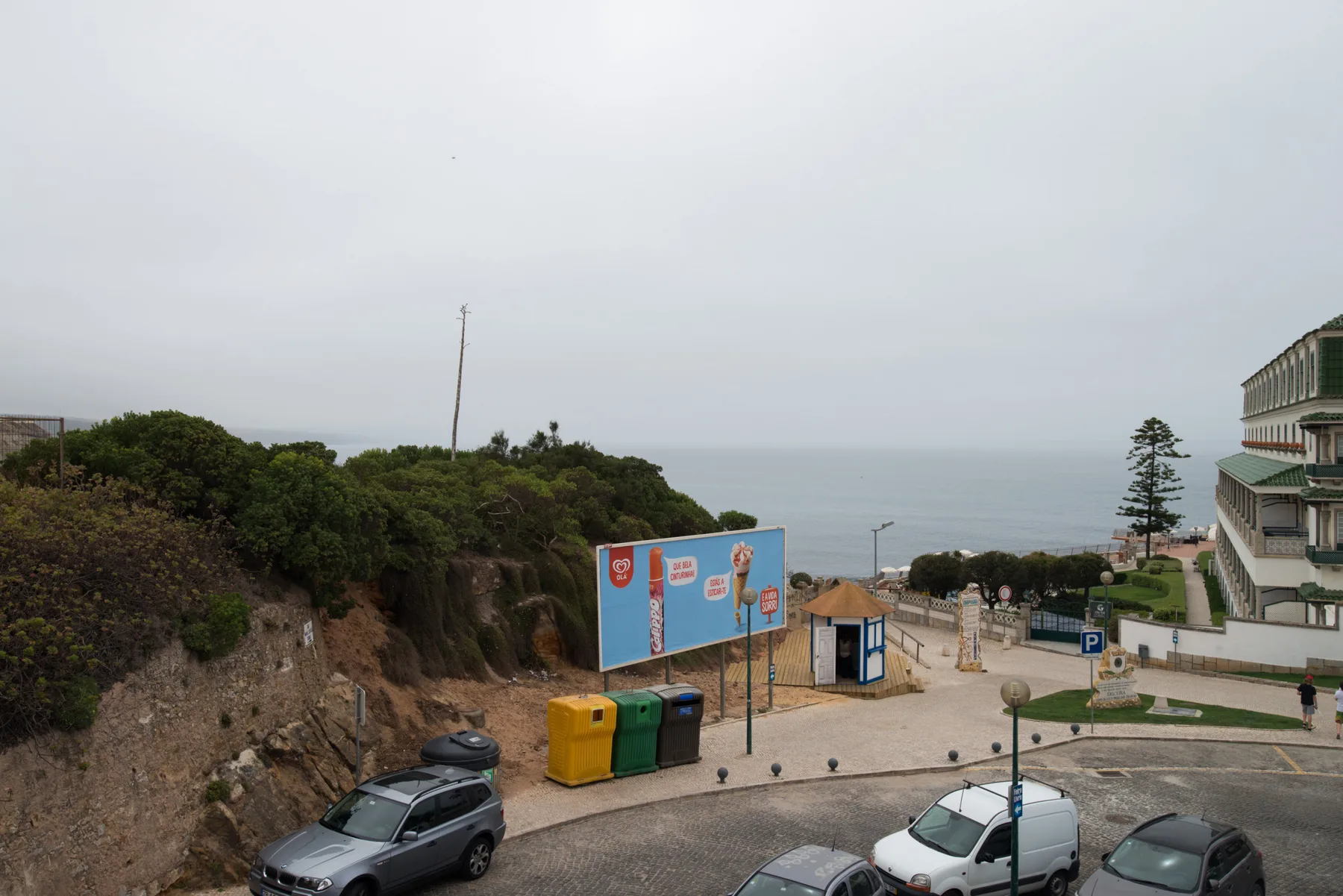 Una carretera costera y una zona de estacionamiento dan al océano junto a una ladera ajardinada.
