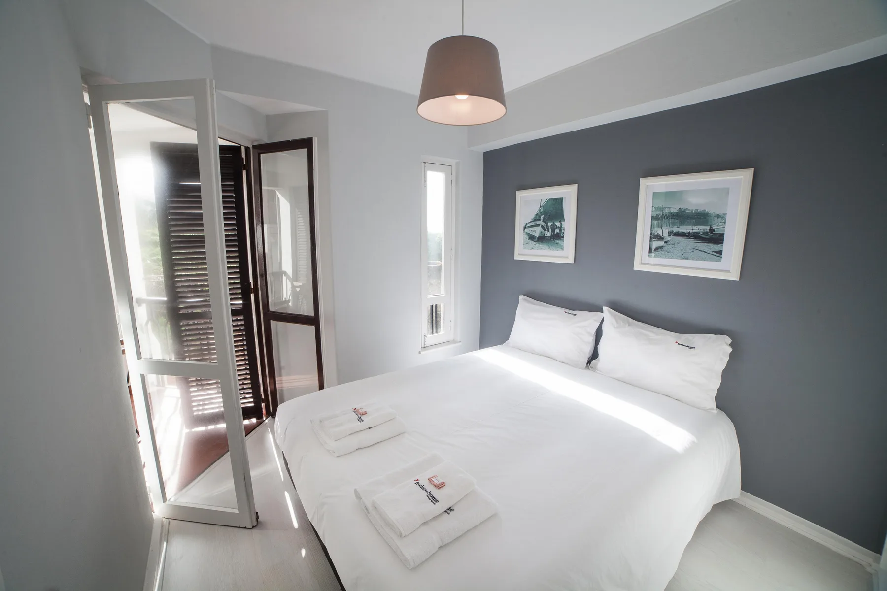 A bright bedroom with white bedding and framed artwork above the bed.