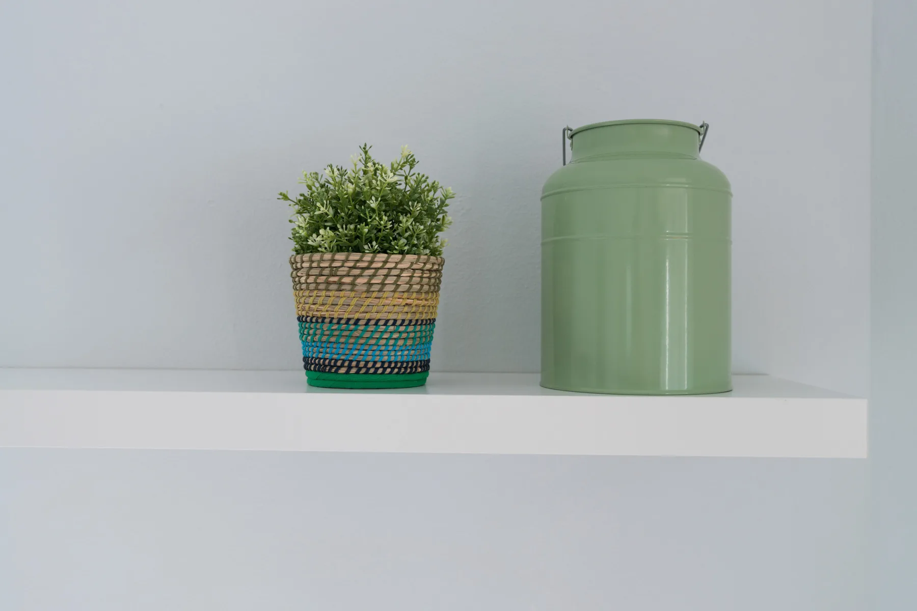 Una pequeña planta en maceta y un recipiente verde están sobre una repisa blanca.