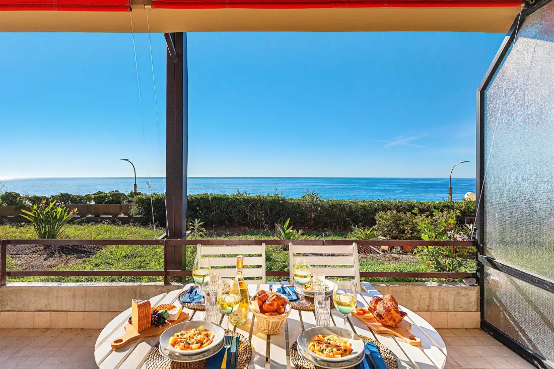 Una mesa con comida y bebidas da a un jardín y al océano.