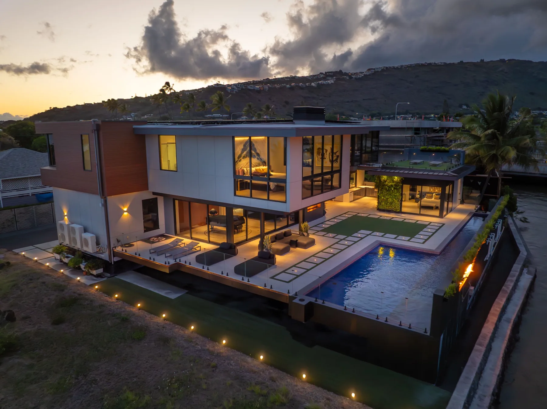 Una casa moderna con grandes ventanales y una piscina al anochecer.