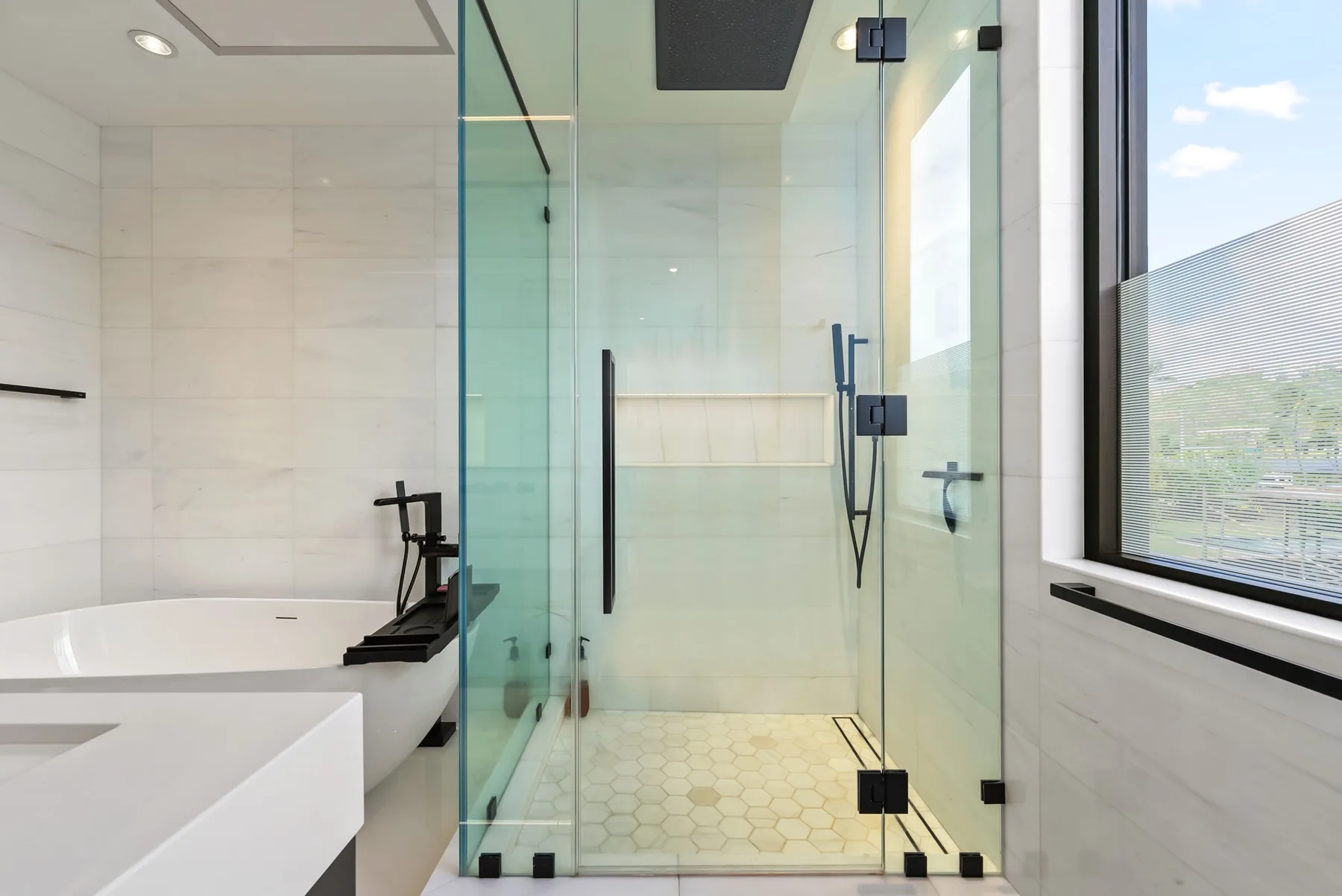 Un baño moderno y luminoso con una ducha de vidrio y una bañera exenta.
