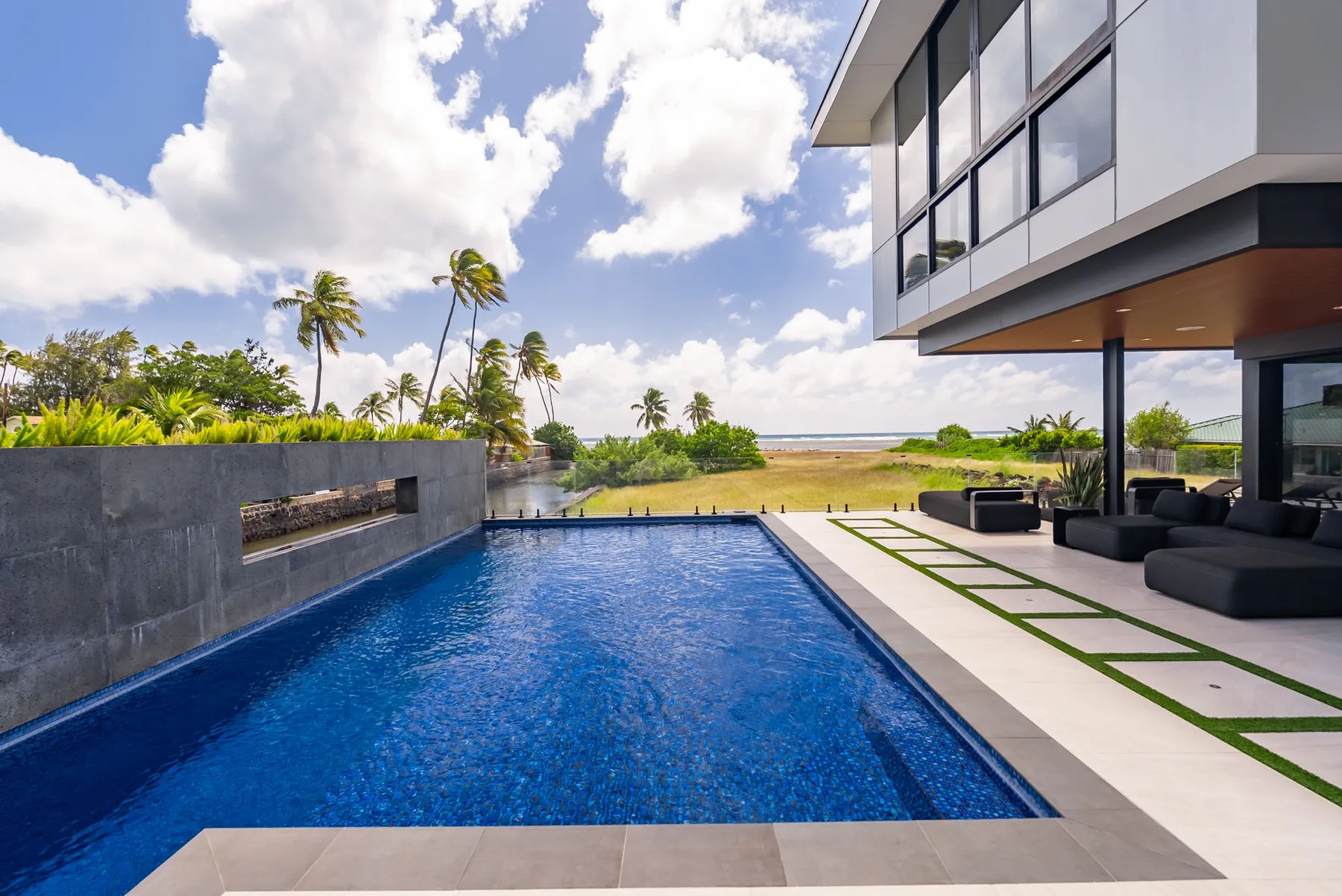 Una piscina exterior junto a una casa moderna, con asientos y palmeras.