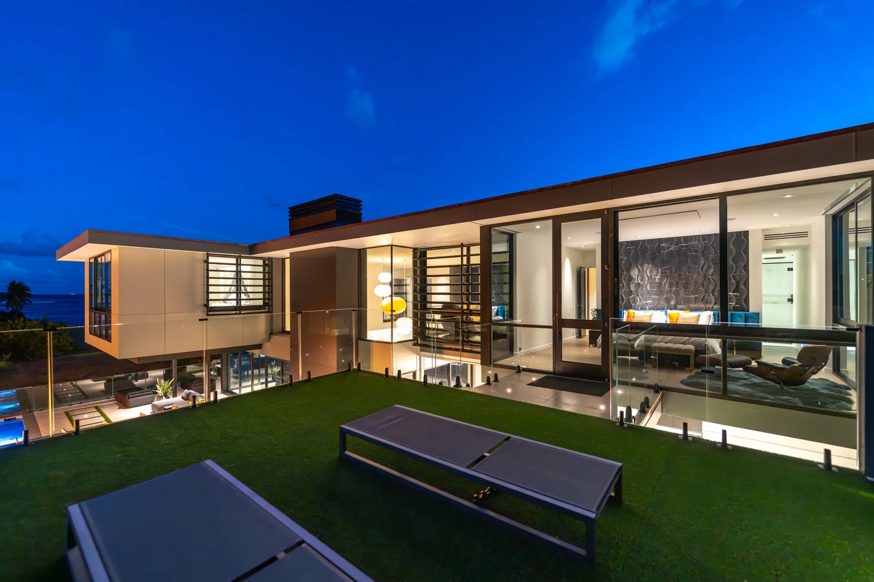 Una casa moderna al atardecer, con amplios ventanales que dan a un césped.
