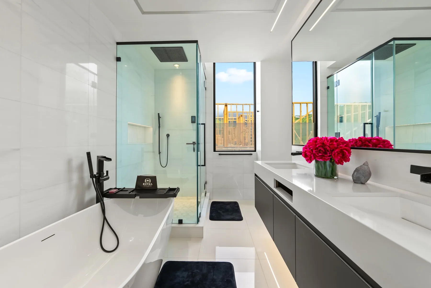 Un baño moderno y luminoso con bañera, ducha de vidrio y un largo lavabo.