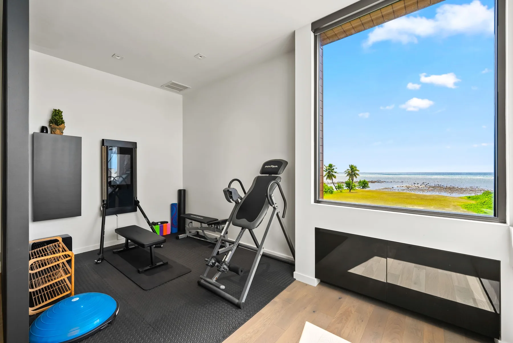Un pequeño gimnasio con equipo de ejercicio junto a una gran ventana con vista a la costa.