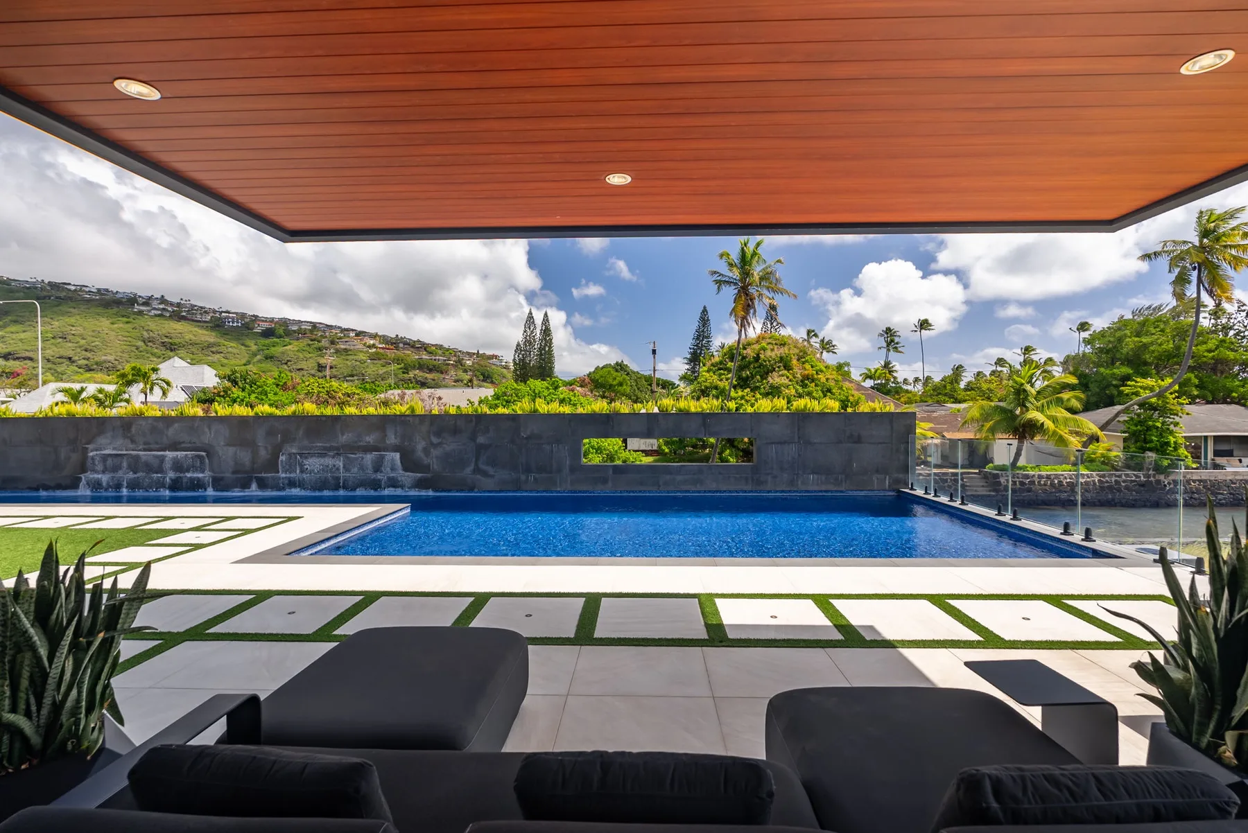 Una piscina al aire libre bajo un patio cubierto, con asientos y vegetación tropical.