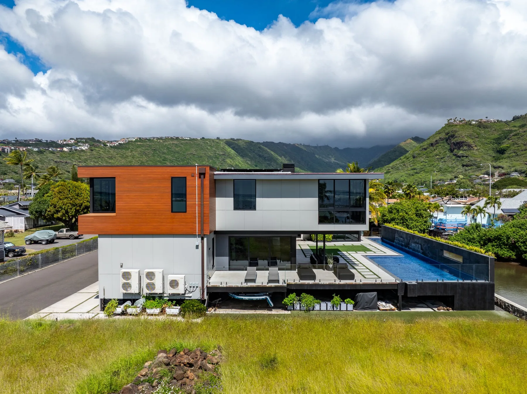 Una casa moderna con piscina se encuentra frente a un paisaje de montañas verdes.