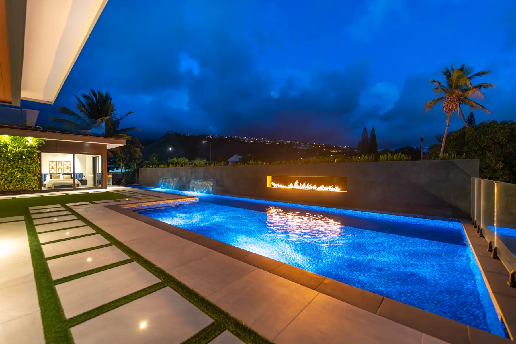Una piscina exterior iluminada junto a un sendero pavimentado por la noche.