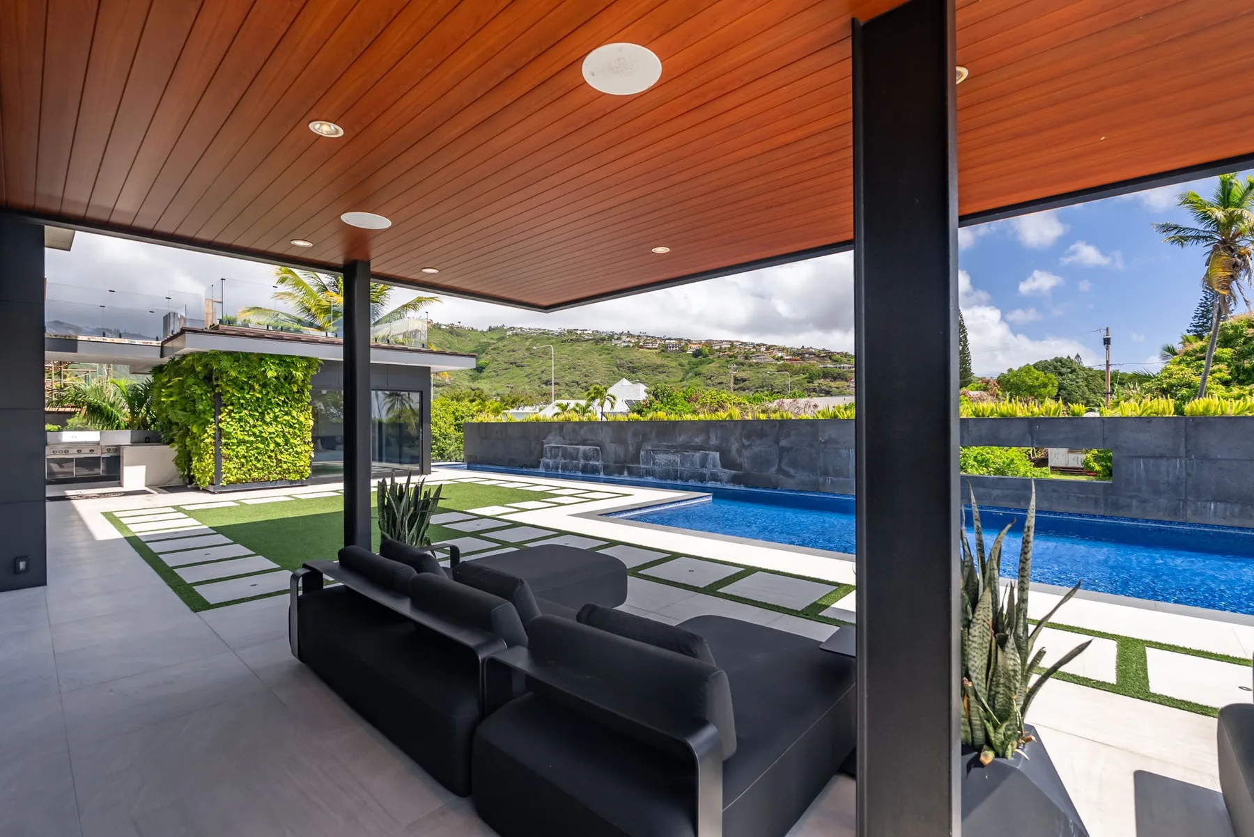 Una sala exterior cubierta con asientos tiene vistas a una piscina y un jardín.