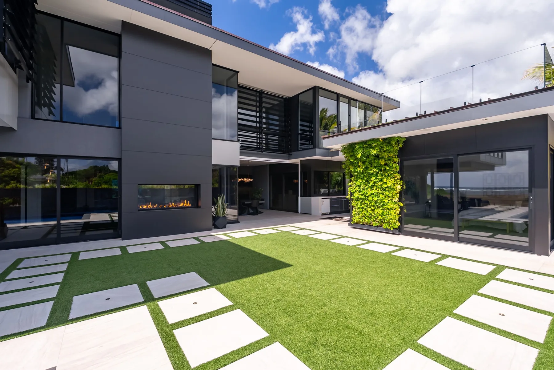 Una casa moderna se abre a un césped verde con grandes losas blancas.