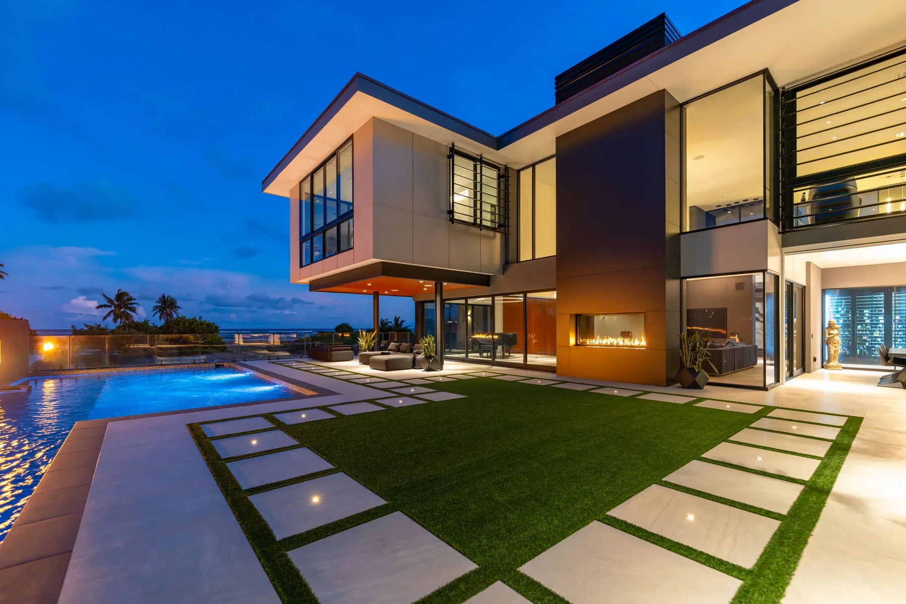 Una casa moderna da a una piscina y un patio con césped al anochecer.