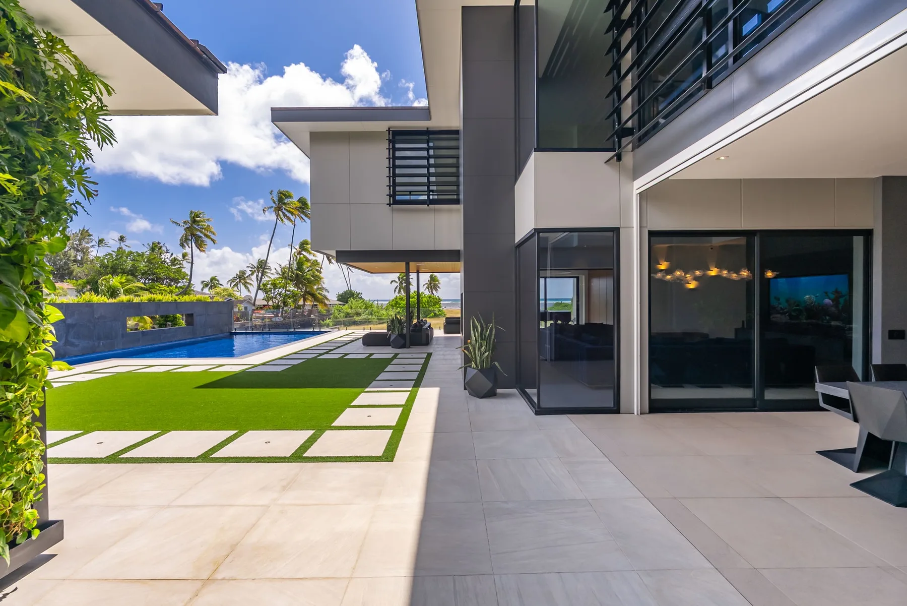 Una casa moderna da a un patio pavimentado junto a un césped y una piscina.