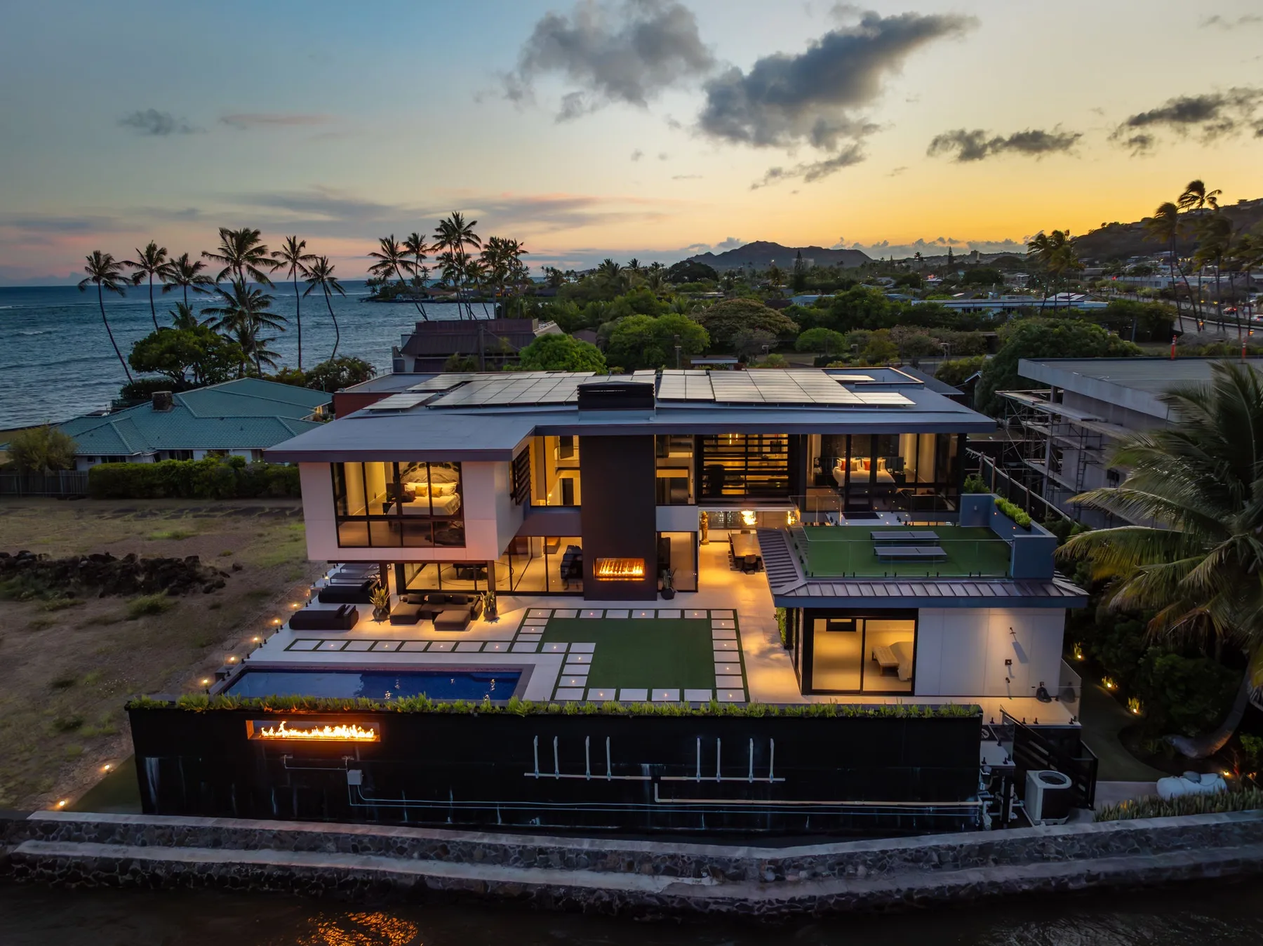 Una casa moderna mira al océano al atardecer, con una piscina iluminada.