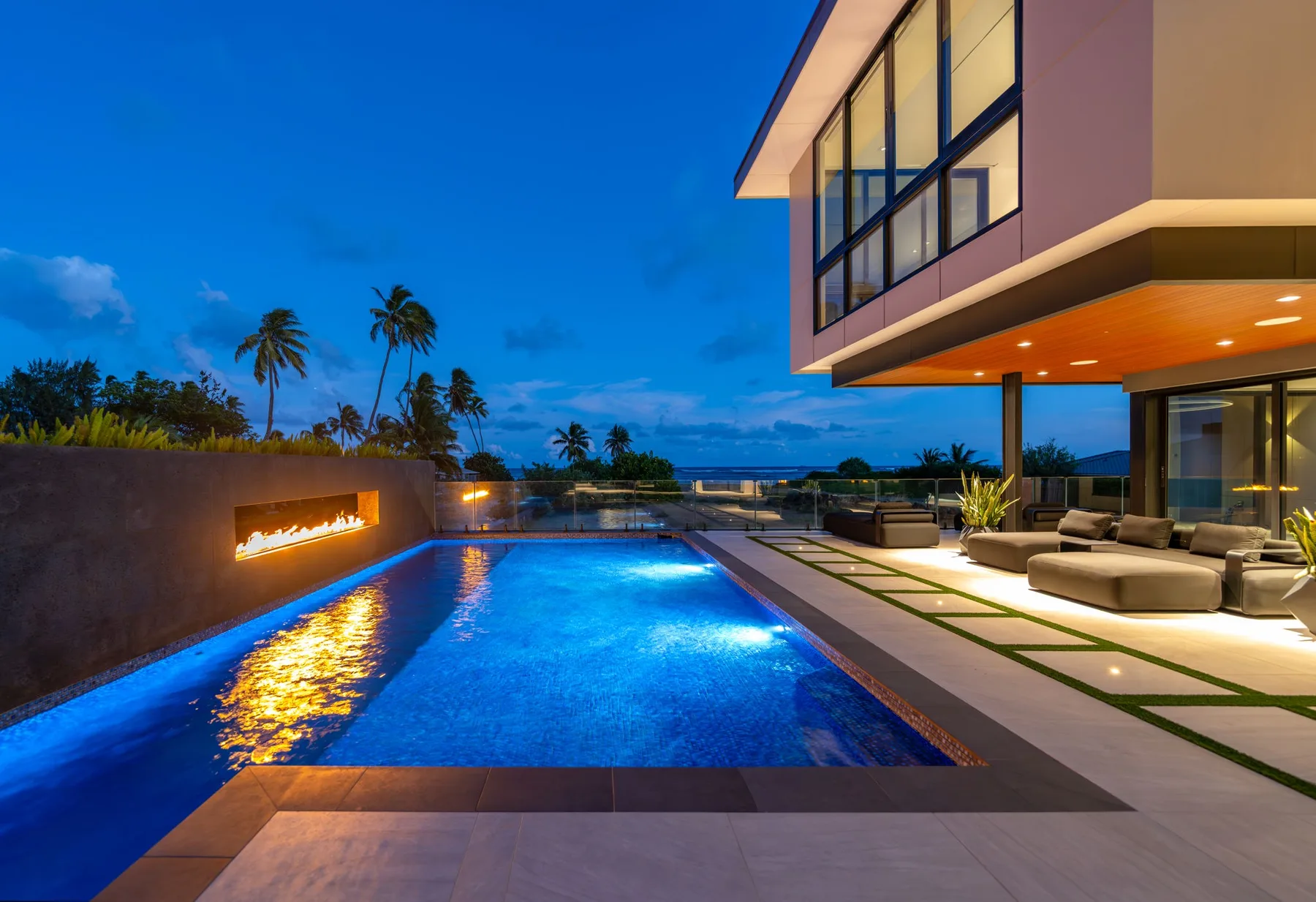 Una casa moderna da a una piscina iluminada y una zona de estar al aire libre al anochecer.