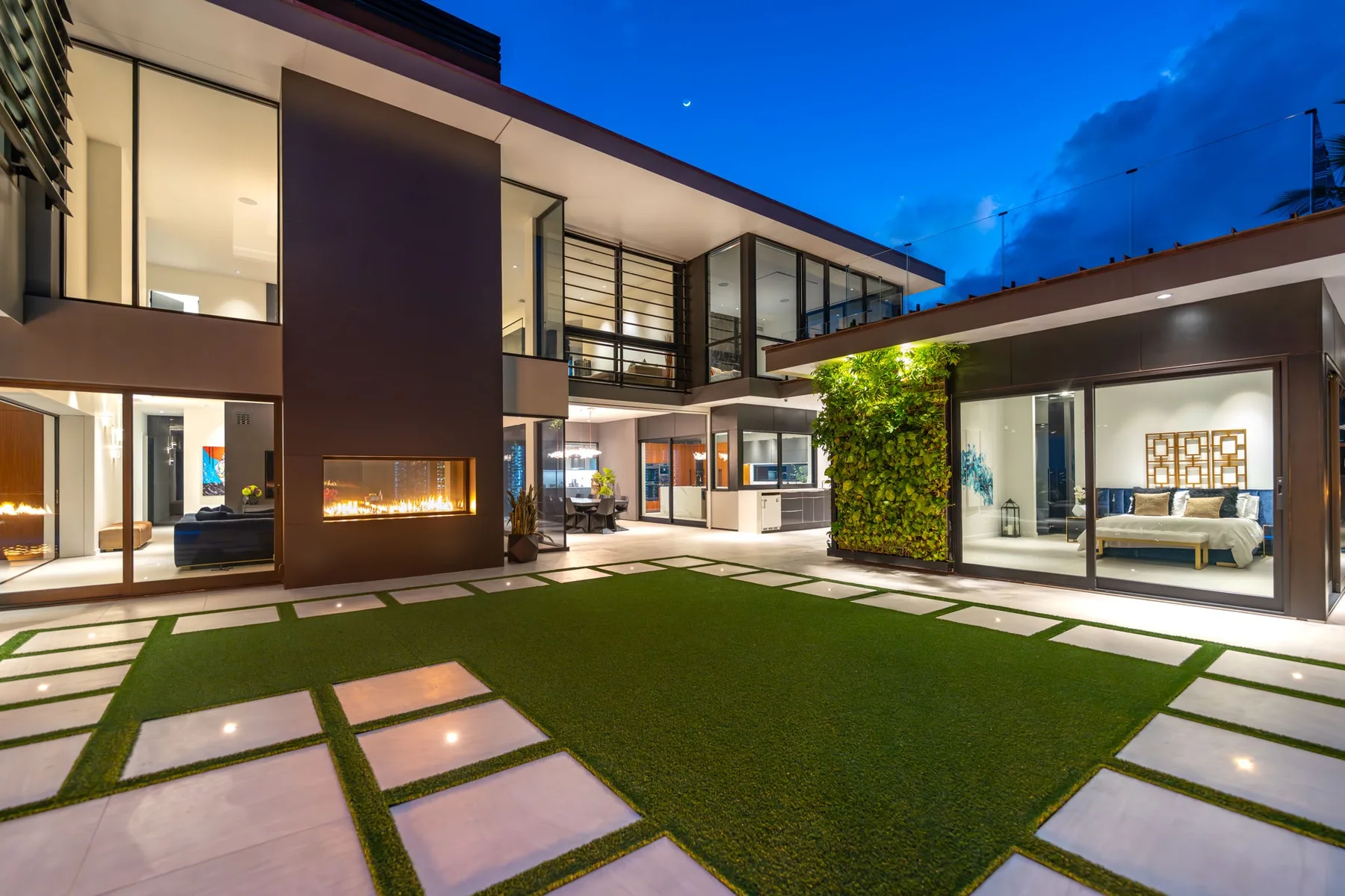 Una casa moderna al anochecer rodea un patio con césped y caminos pavimentados.