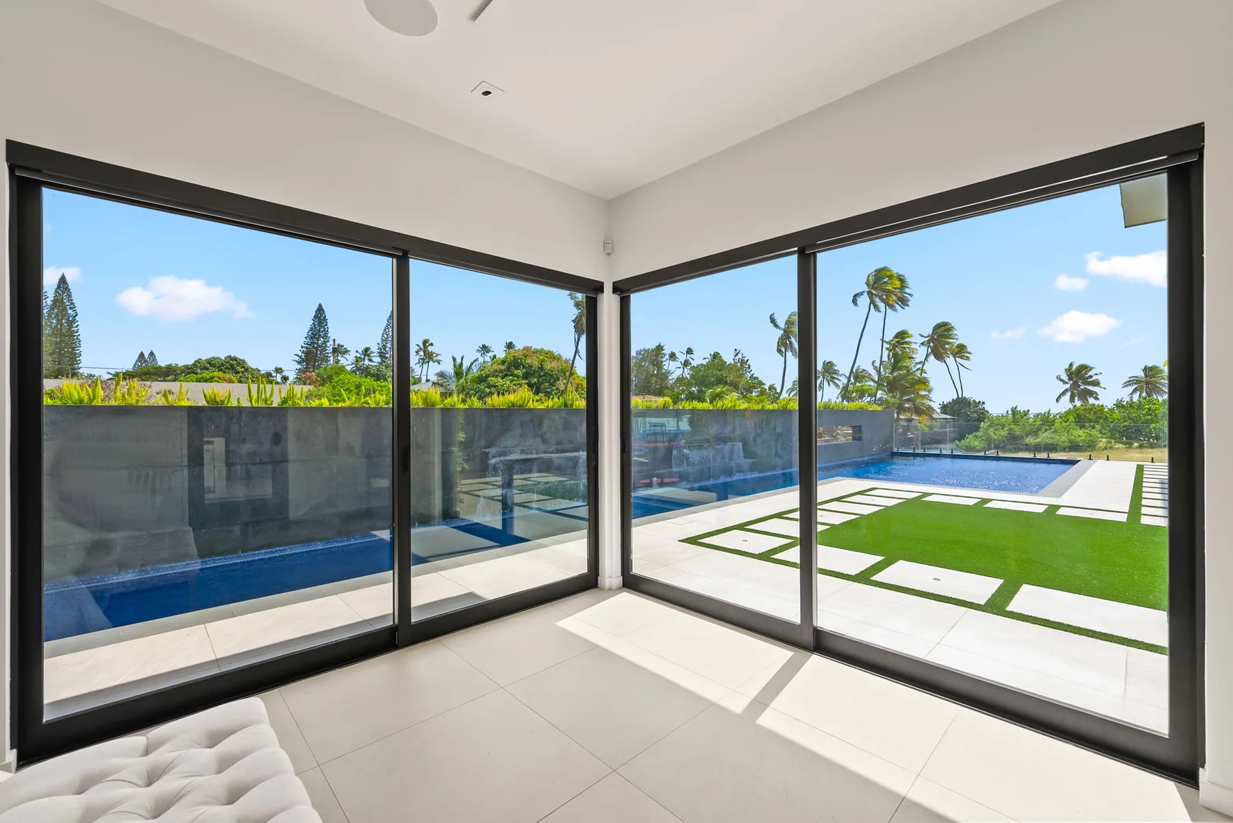 Una habitación luminosa con ventanales que dan a una piscina y un césped.