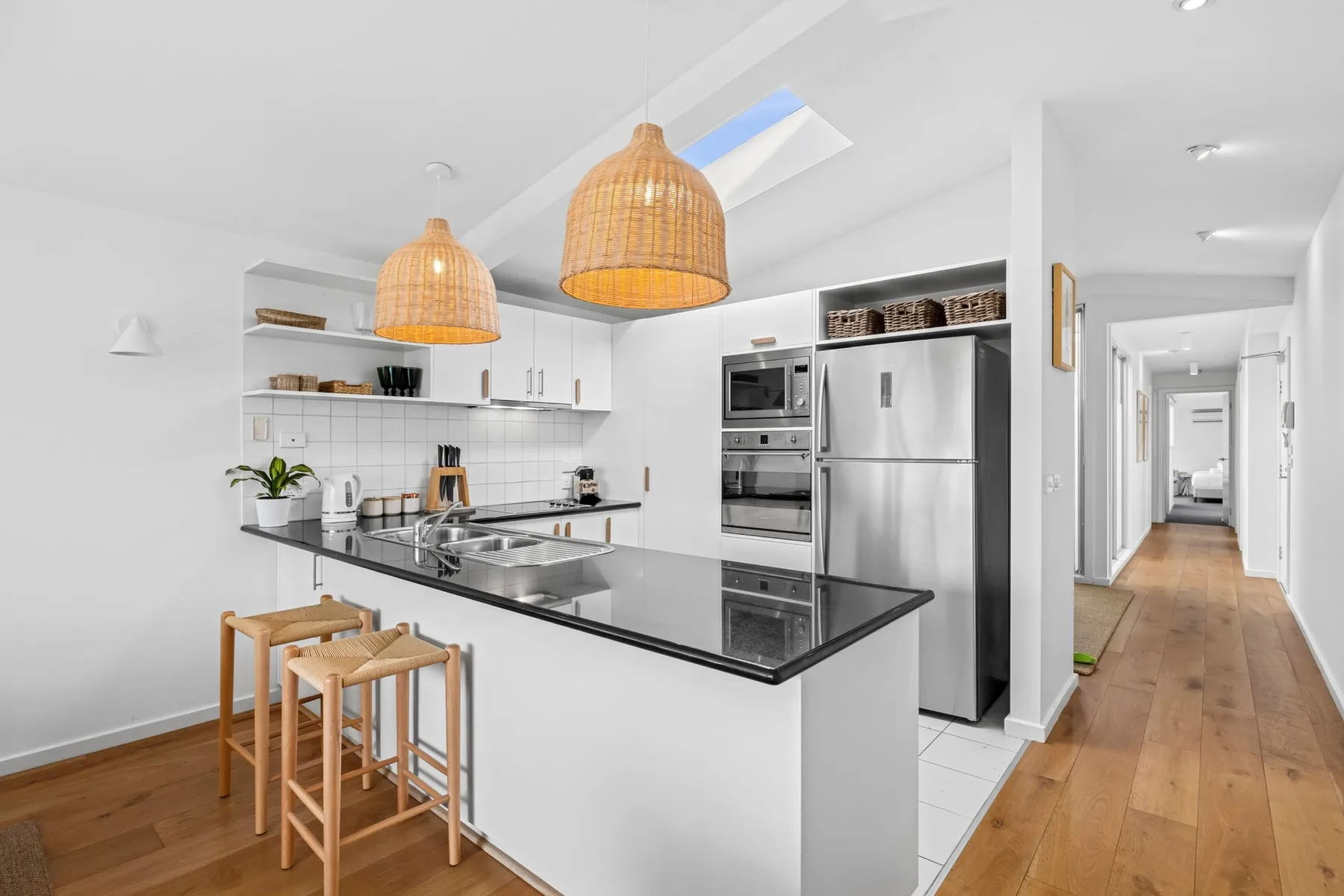 A bright kitchen with a central island, pendant lights, and a hallway beyond.