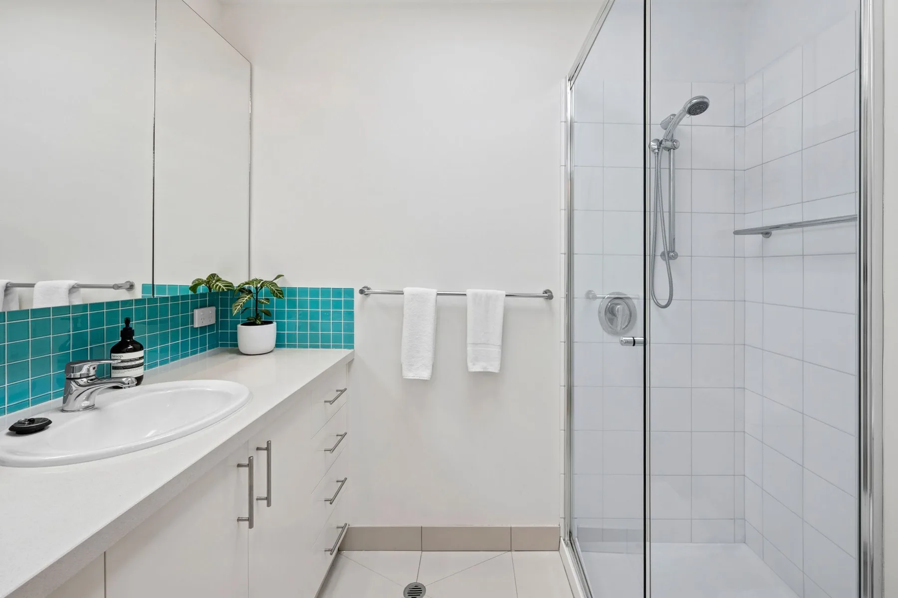 A bright bathroom with a white vanity and glass-enclosed shower.