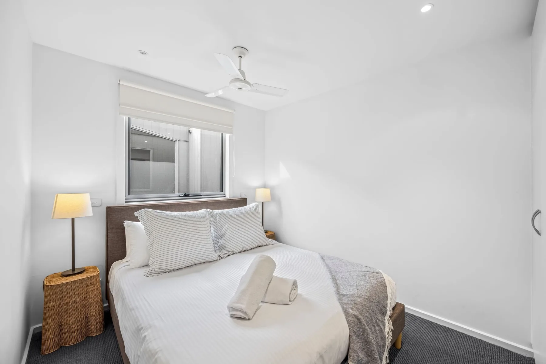 A bright bedroom with a neatly made bed beneath a window.
