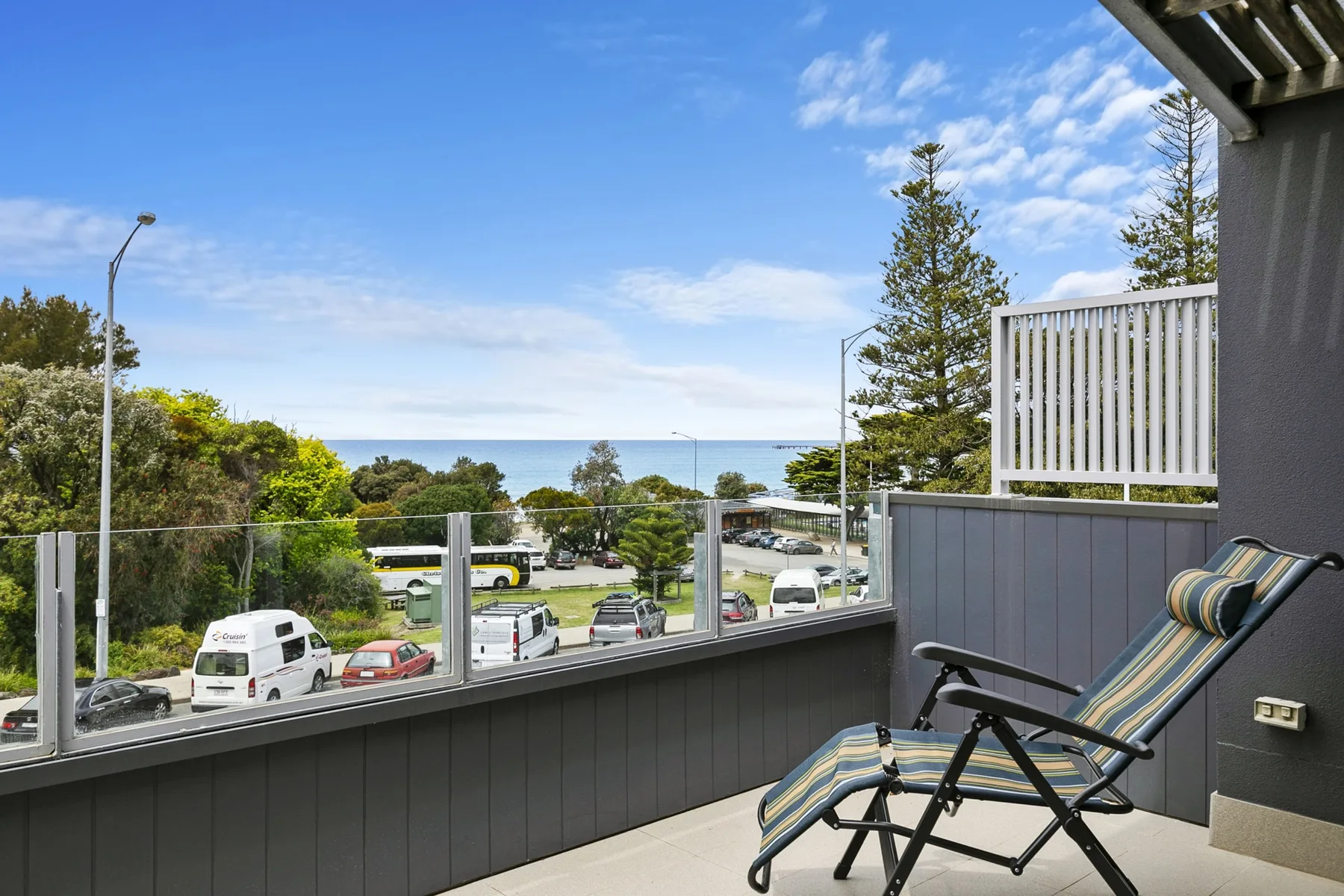 A balcony seating area overlooks a coastal view and nearby trees.
